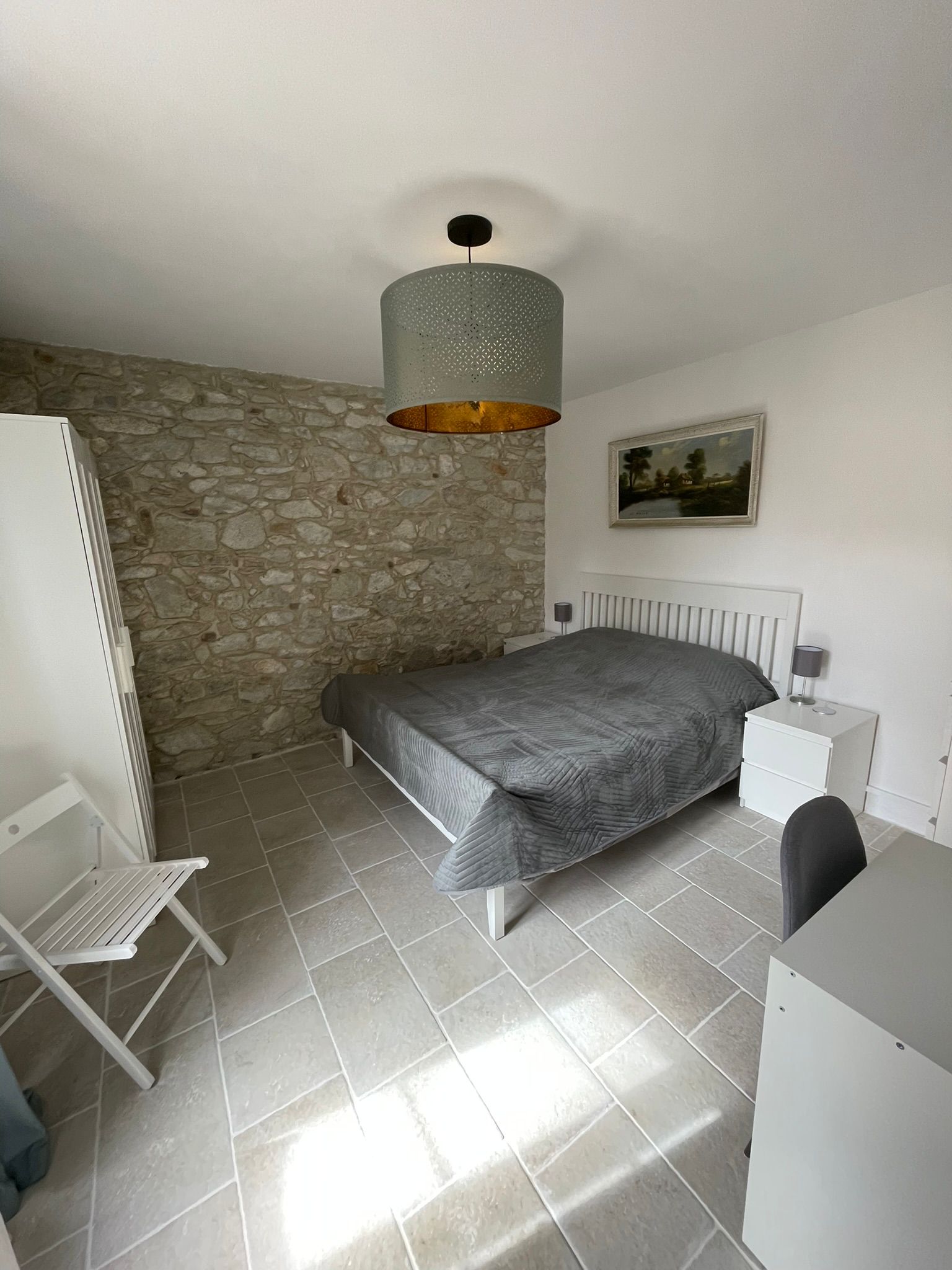 Lichte slaapkamer met stenen accentmuur en grijs bed